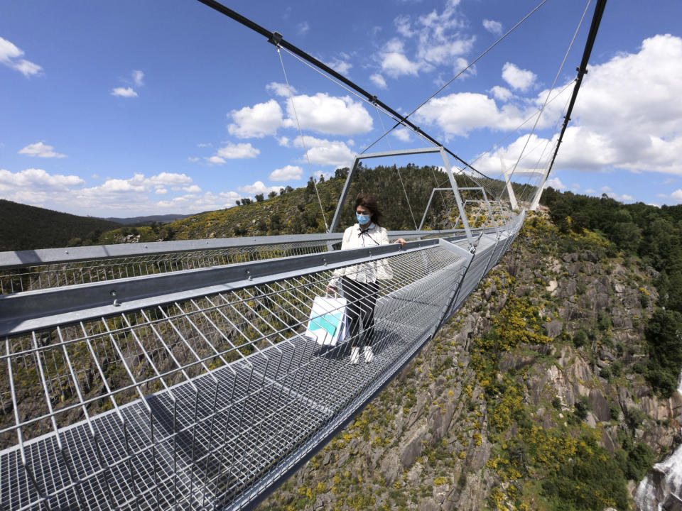 A woman walks across a narrow footbridge suspended across a river canyon, which claims to be the world's longest pedestrian bridge, in Arouca, northern Portugal, Sunday, May 2, 2021. The Arouca Bridge inaugurated Sunday, offers a half-kilometer (almost 1,700-foot) walk across its span, some 175 meters (574 feet) above the River Paiva. (AP Photo/Sergio Azenha)