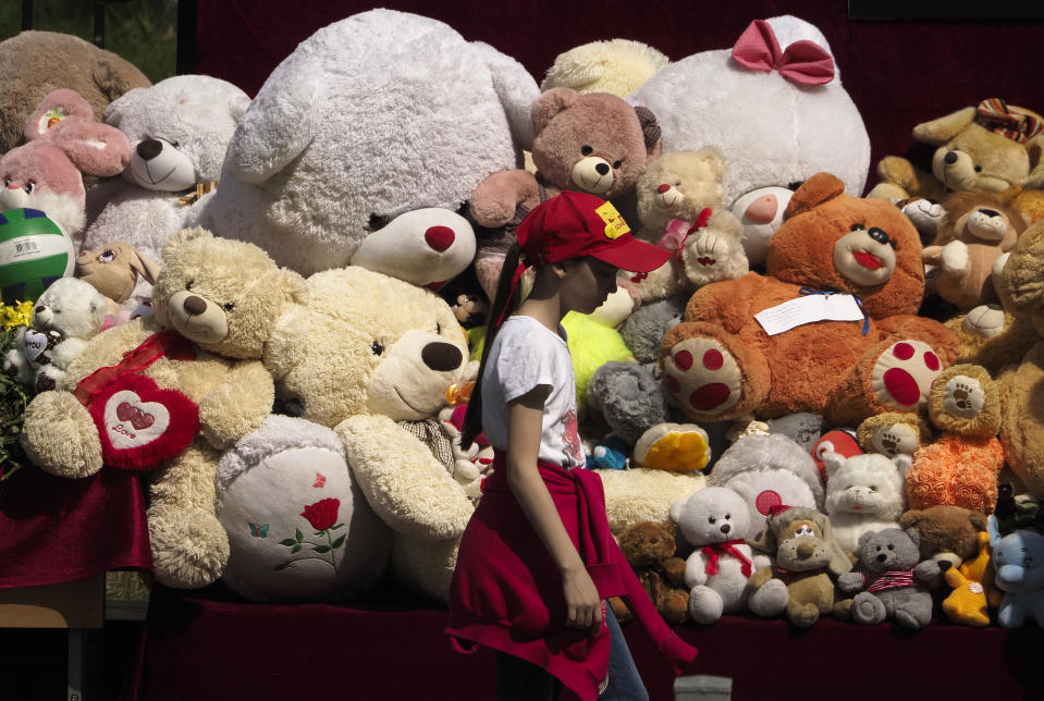 A girl walks past toys brought by people near a school after a shooting on Tuesday in Kazan, Russia, Thursday, May 13, 2021. Russian officials say a gunman attacked a school in the city of Kazan and Russian officials say several people have been killed. Officials said the dead in Tuesday's shooting include students, a teacher and a school worker. Authorities also say over 20 others have been hospitalised with wounds. (AP Photo/Dmitri Lovetsky)