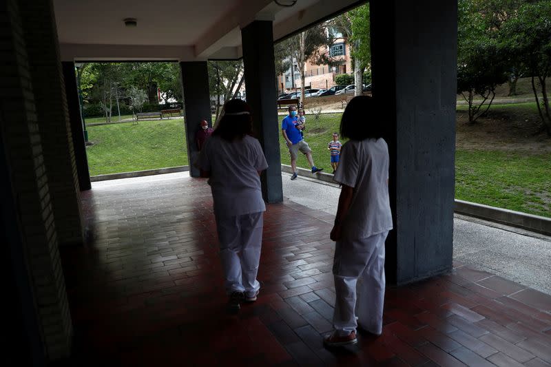 People look at Comunidad de Madrid home care nurses Maria Jesus Santamaria and Ana Arenal as they arrive at an apartment complex to treat a COVID-19 patient in Madrid
