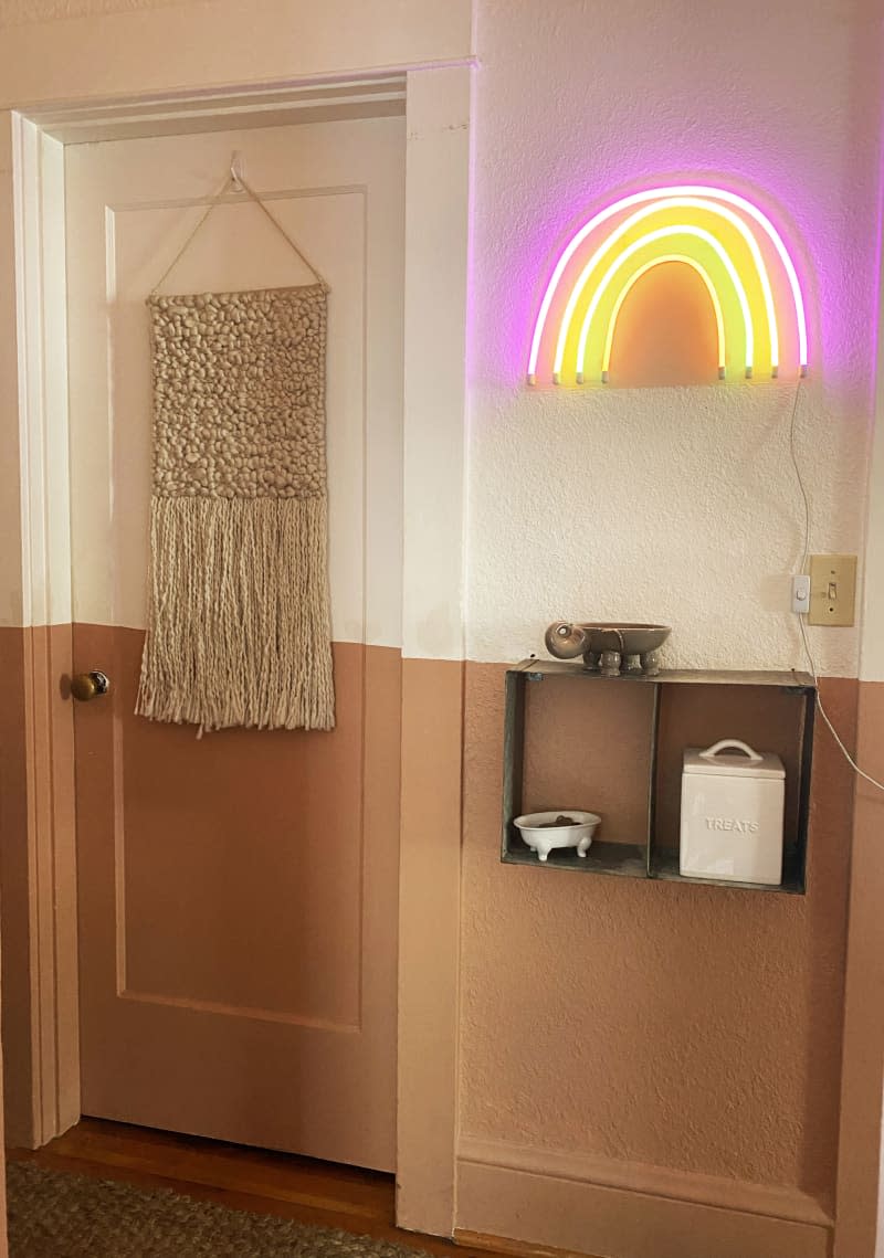 Hallway with half painted terra cotta bottom, with a neon rainbow light hanging on the wall