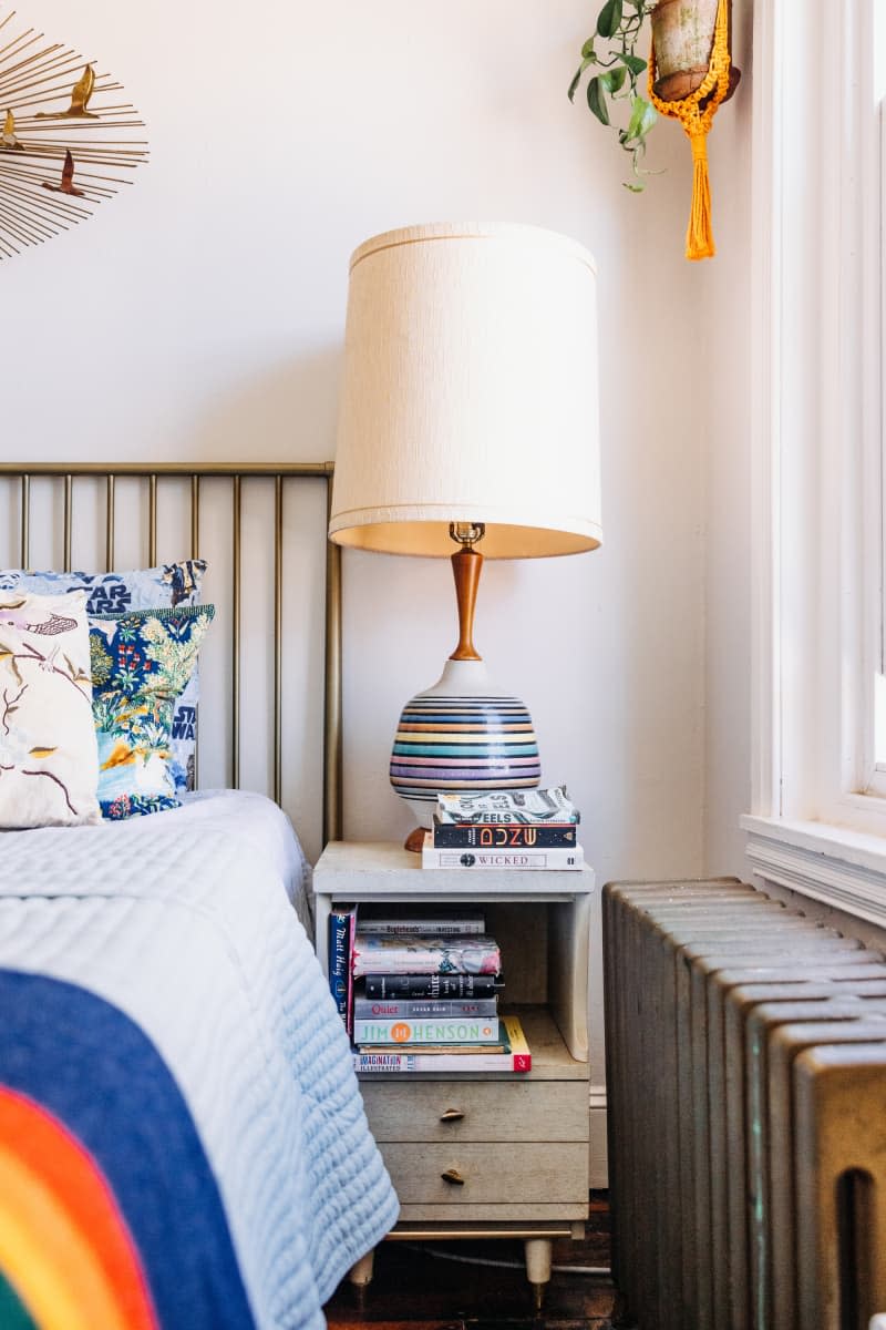 Nightstand with books and a colorful large lamp.