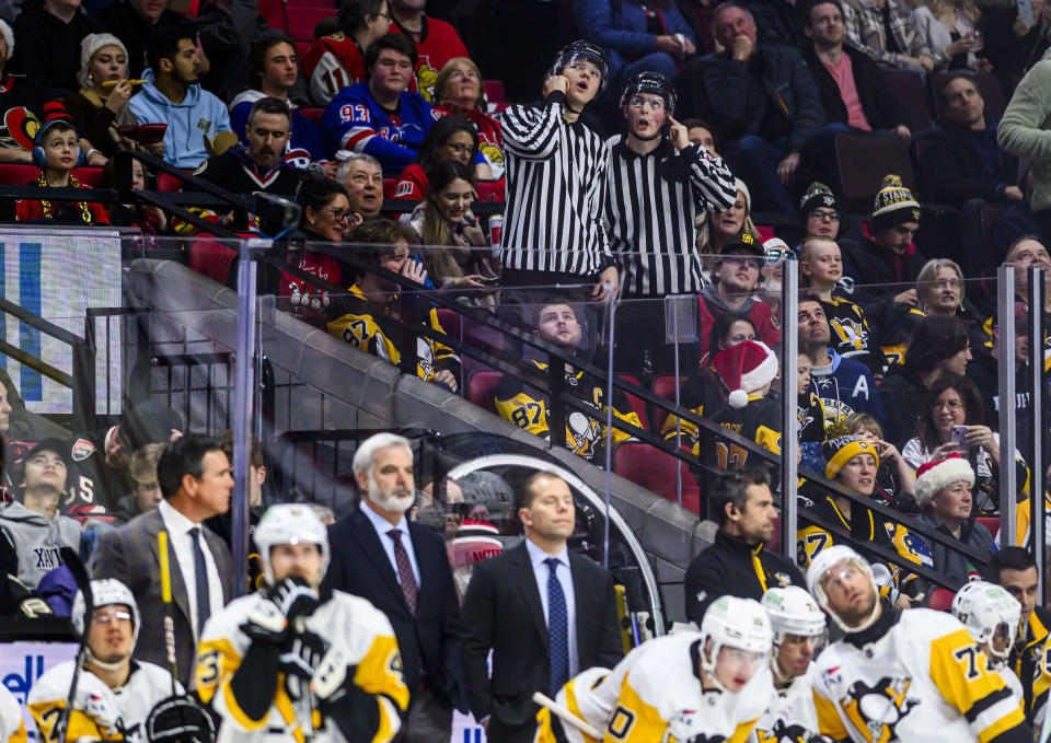 Fans dressed in referee uniforms mimic on-ice officials as they review a goal by Ottawa Senators' Erik Brannstrom after a Pittsburgh Penguins coach's challenge during the second period of an NHL hockey game in Ottawa, Ontario, on Saturday, Dec. 23, 2023. (Justin Tang/The Canadian Press via AP)