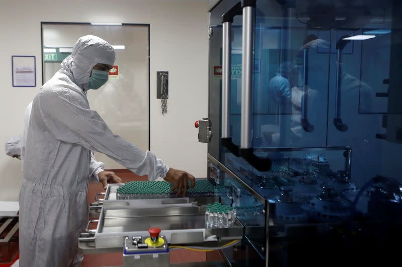 An employee in personal protective equipment (PPE) removes vials of AstraZeneca's COVISHIELD, coronavirus disease (COVID-19) vaccine from a visual inspection machine inside a lab at Serum Institute of India, in Pune