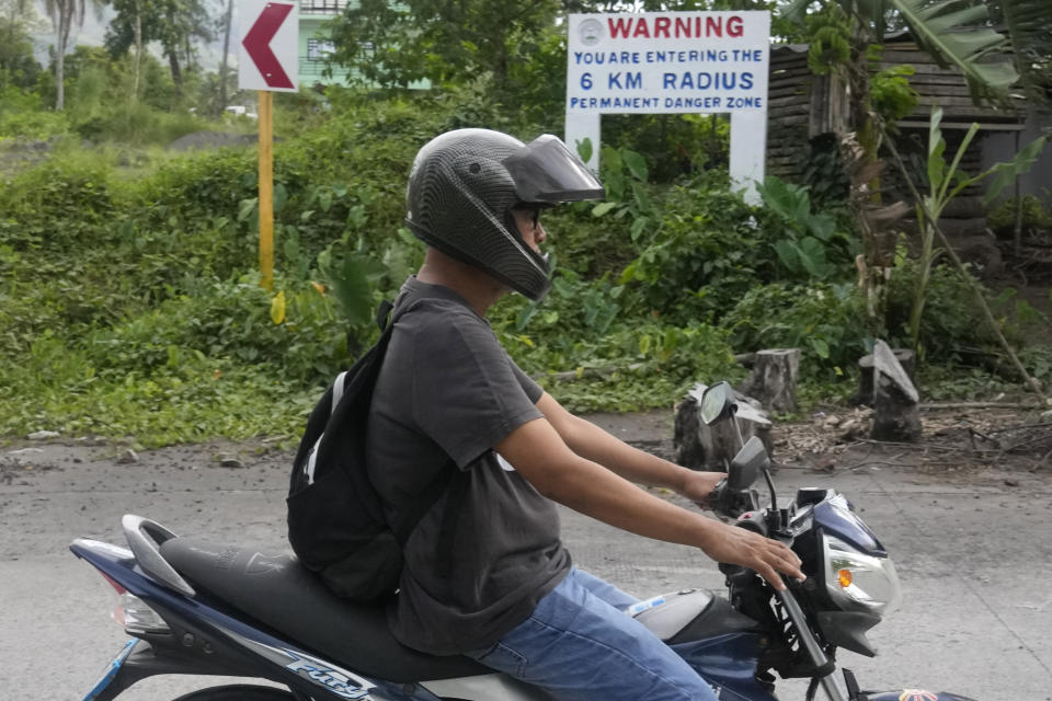 A man passes by a warning sign along a road in Mabinit, located near Mayon volcano, Legaspi, Albay province, northeastern Philippines, Saturday, June 10, 2023. Monsoon rains that could be unleashed by an offshore typhoon were complicating worries of villagers threatened by a restive Philippine volcano that has forced thousands of people to flee from their homes.(AP Photo/Aaron Favila)