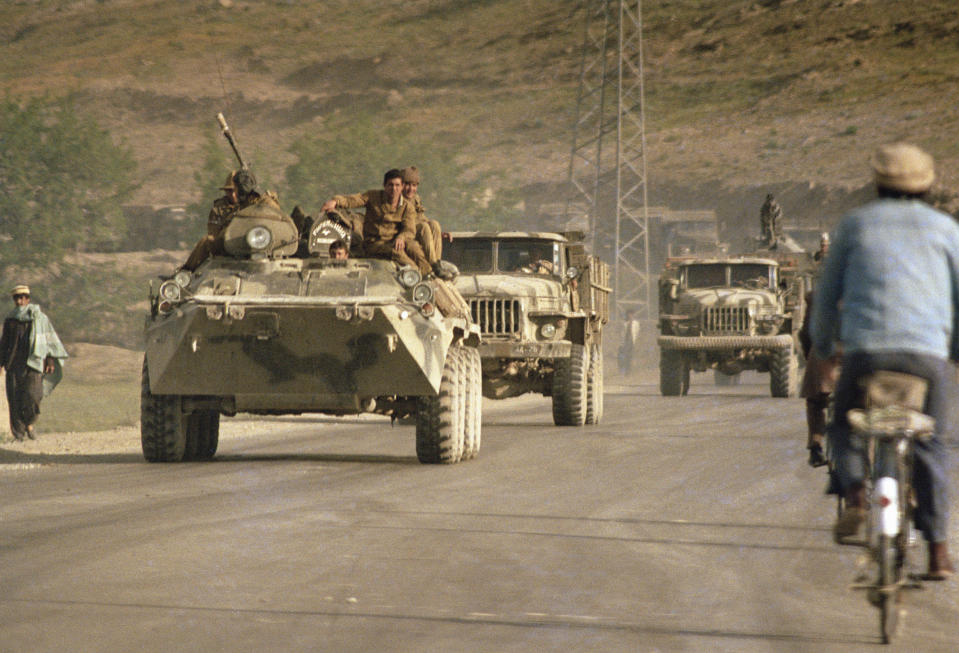 FILE - In this April 23, 1988 file photo, an Afghan cyclist passes by a Soviet military convoy led by an armored personnel carrier on the highway leading to Kabul The Soviet troops will begin its first phrase of withdrawal on May 15. Afghanistan is marking the 31st anniversary of the Soviet Union's last soldier leaving the country, Saturday, Feb. 15, 2020. This year's anniversary comes as the United States negotiates its own exit after 18 years of war, America's longest. (AP Photo/Liu Heung Shing, File)