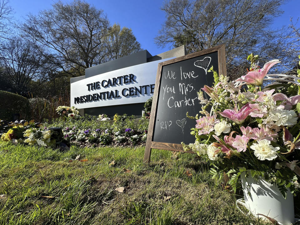 Bouquets of flowers and a sign in tribute to Rosalynn Carter are seen at The Carter Presidential Center in Atlanta, on Monday, Nov. 27, 2023. The former U.S. first lady died on Nov. 19, 2023. She was 96. (AP Photo/Ron Harris)