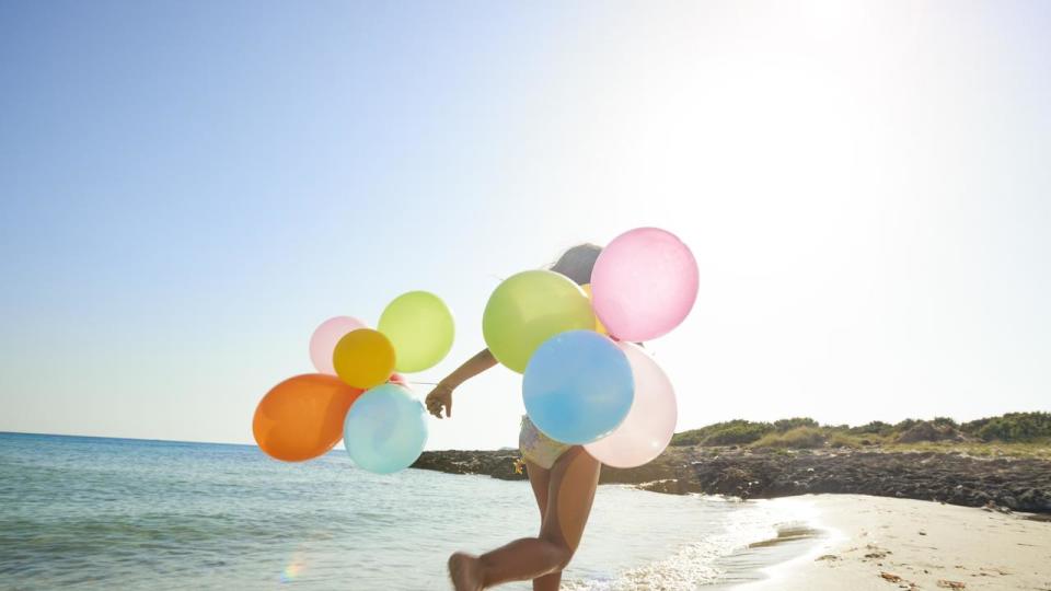 Little girl running with balloons on the beach