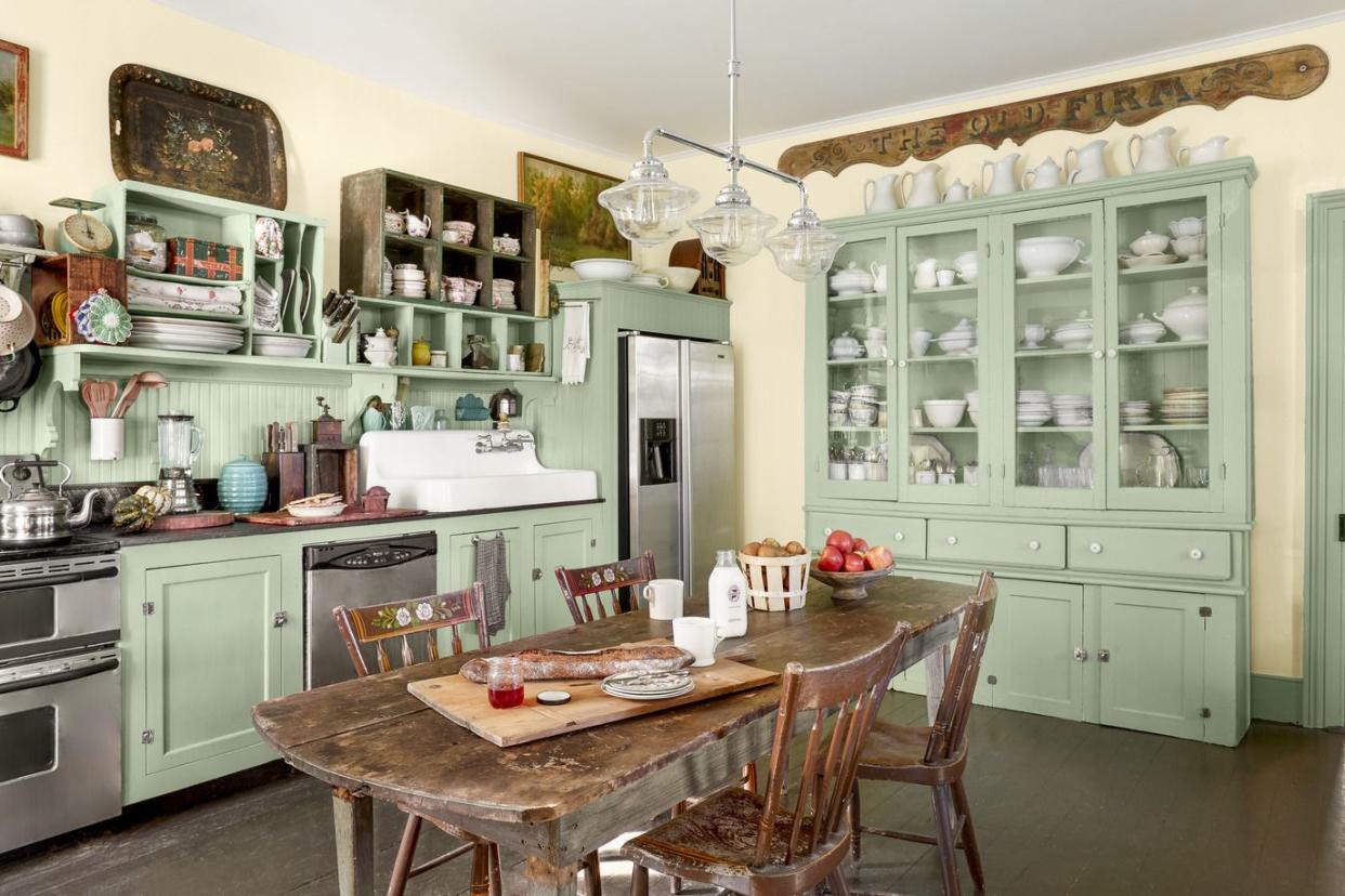 a kitchen with mint green painted cabinets and a collection of white dishes and a table in the middle