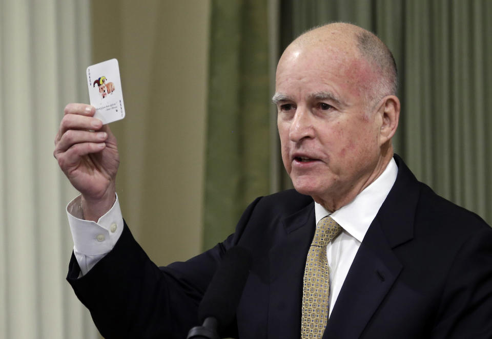 Gov. Jerry Brown displays a playing card with his dog, Sutter, on it as he gives the annual State of the State speech before a joint session of the Legislature at the Capitol in Sacramento, Calif., Wednesday, Jan. 22, 2014. Brown delivered a dual message in his annual address to the Legislature, that a California resurgence is well underway but is threatened by economic and environmental uncertainties. On the backside of the playing card is a chart showing how high deficits follow balanced budgets, and warned that even though there is a budget surplus, lawmakers should not overspend.(AP Photo/Rich Pedroncelli)