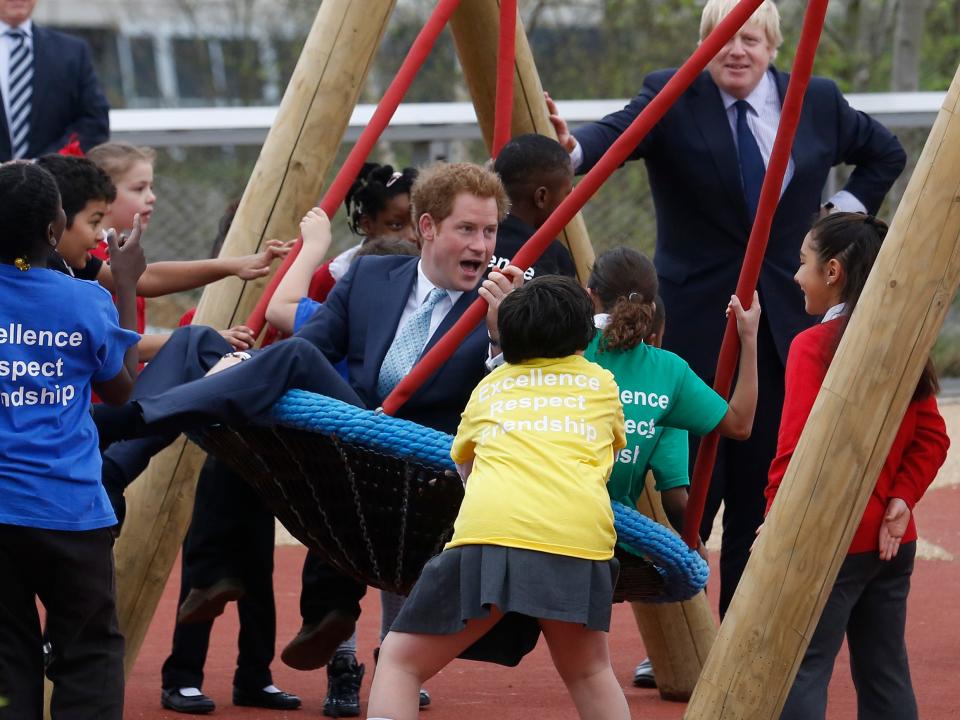 Prince Harry is pushed on a swing by a group of children