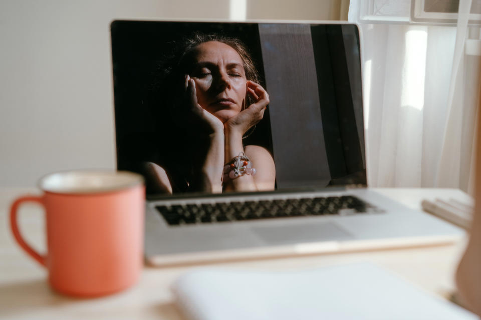 Woman resting face on hands, looking pensive, with a coffee mug beside the computer