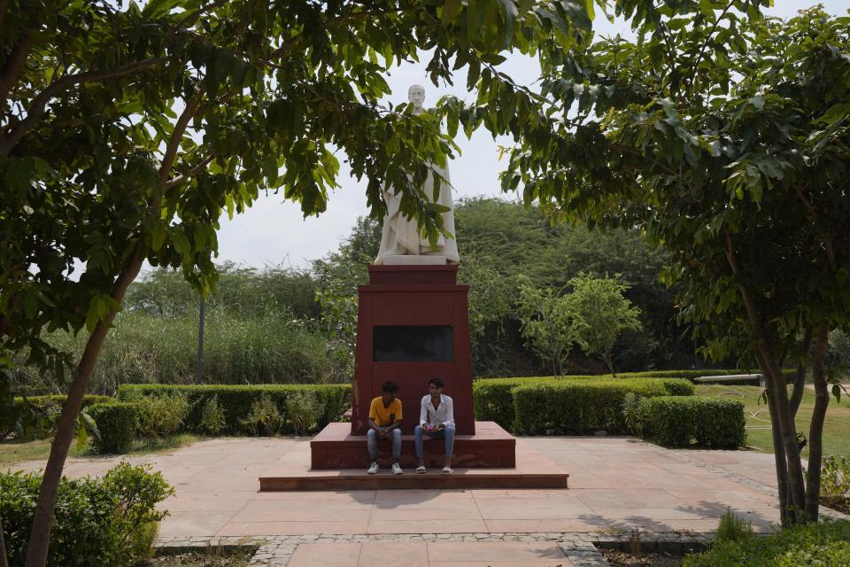 People sit under a British king's statue in coronation park, which houses statues of old British Kings and rulers in New Delhi, Sunday, Sept. 11, 2022. India, once the largest of Britain’s colonies that endured two centuries of imperial rule has moved on. Queen Elizabeth II’s death provoked sympathies from some while for a few others, it jogged memories of a bloody history under the British crown. Among most regular Indians, the news was met with an indifferent shrug. (AP Photo/Manish Swarup)