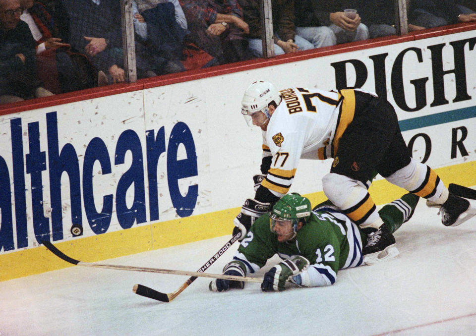 FILE - In this Dec. 13, 1990 file photo, Boston Bruins defenseman Ray Bourque (77) reaches over the back of Hartford Whaler Dean Evason (12) trying to get to the puck behind Boston's goal during first period action in the Boston. The NHL hasn't had best-of-five playoff series since 1986. That's changing for this year with the league expanding to 24 playoff teams as part of its restart. The qualifying round will feature 16 teams facing off in best-of-five series to determine who moves on. (AP Photo/Stephan Savoia, File)