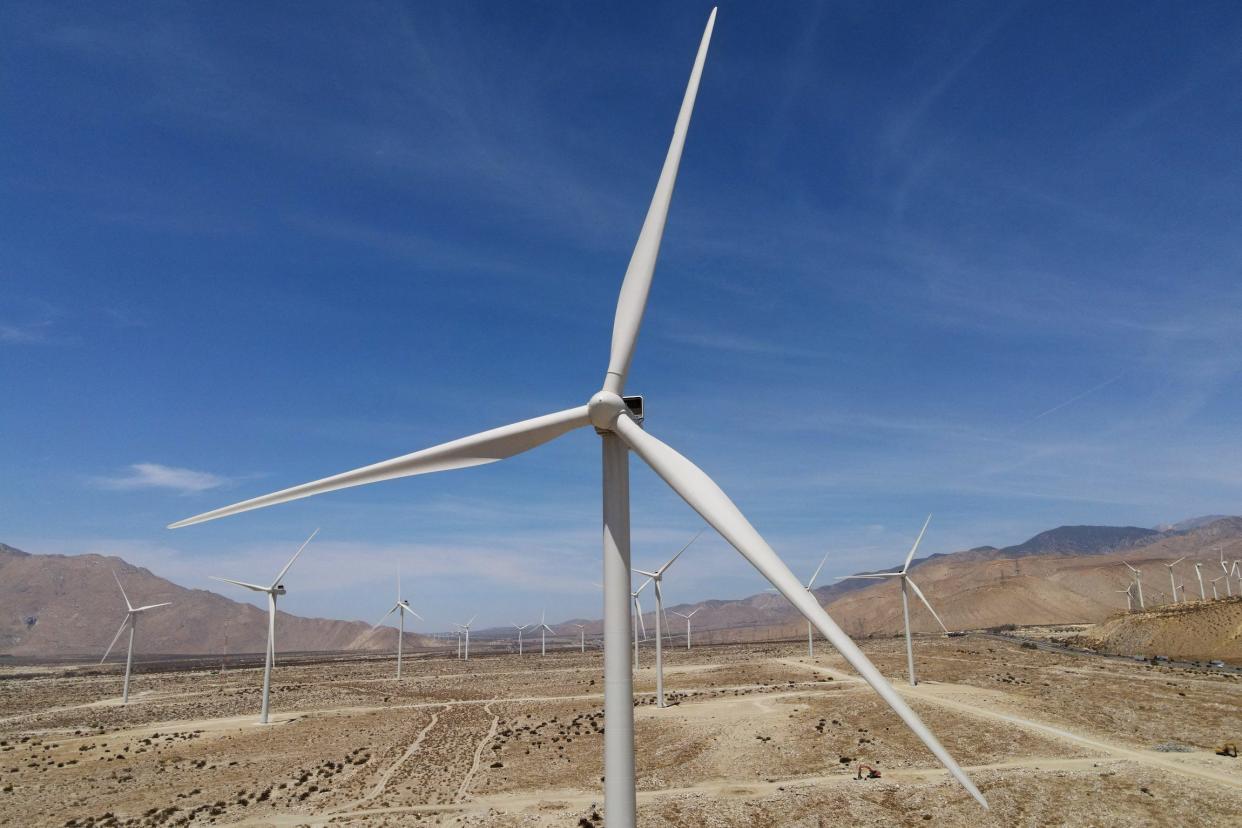 wind turbine in a field of turbines against blue sky mountains in the background