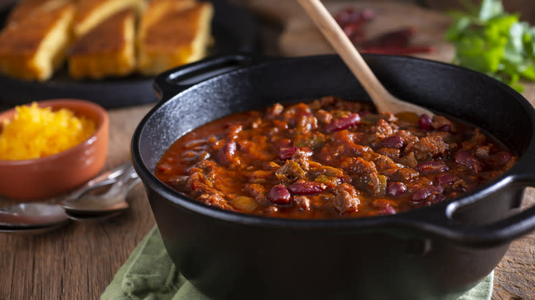 Pot of chili with cheese and cornbread in background