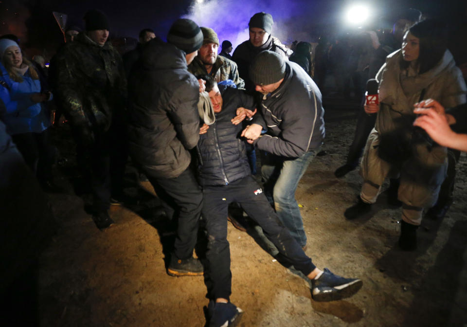 Protesters help another protester, who planned to stop buses carrying passengers evacuated from the Chinese city of Wuhan, outside Novi Sarzhany, Ukraine, Thursday, Feb. 20, 2020. Several hundred residents in Ukraine's Poltava region protested to stop officials from quarantining the evacuees in their village because they feared becoming infected. Demonstrators put up road blocks and burned tires, while Ukrainian media reported that there were clashes with police, and more than 10 people were detained. (AP Photo/Efrem Lukatsky)