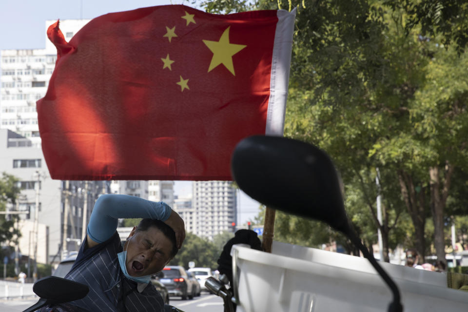A delivery man yawns near a national flag in Beijing on Wednesday, Sept. 2, 2020. China's Ministry of Commerce on Saturday, Sept. 19 2020 issued regulations for its "unreliable entity" list, aimed at foreign companies it says endanger its national sovereignty, security or development interests. (AP Photo/Ng Han Guan)