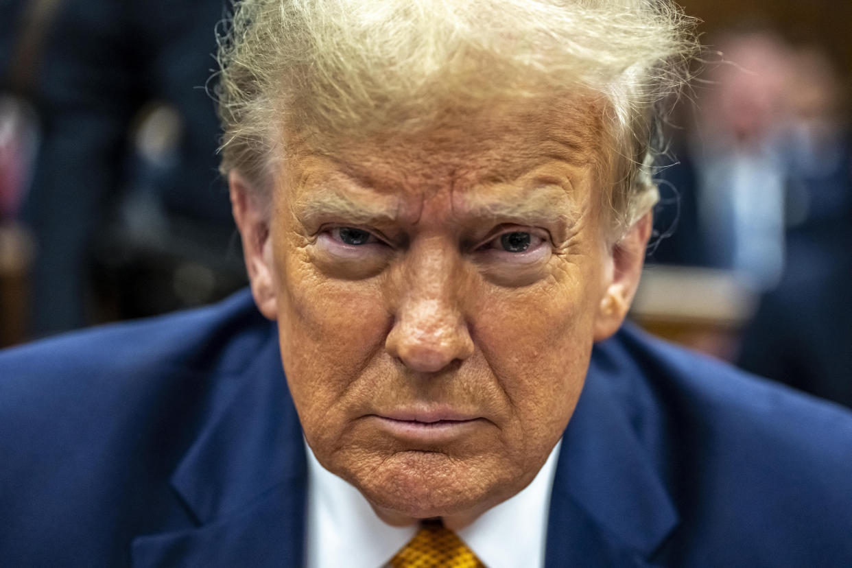 Former President Donald Trump, looking at the camera, sits in the courtroom.