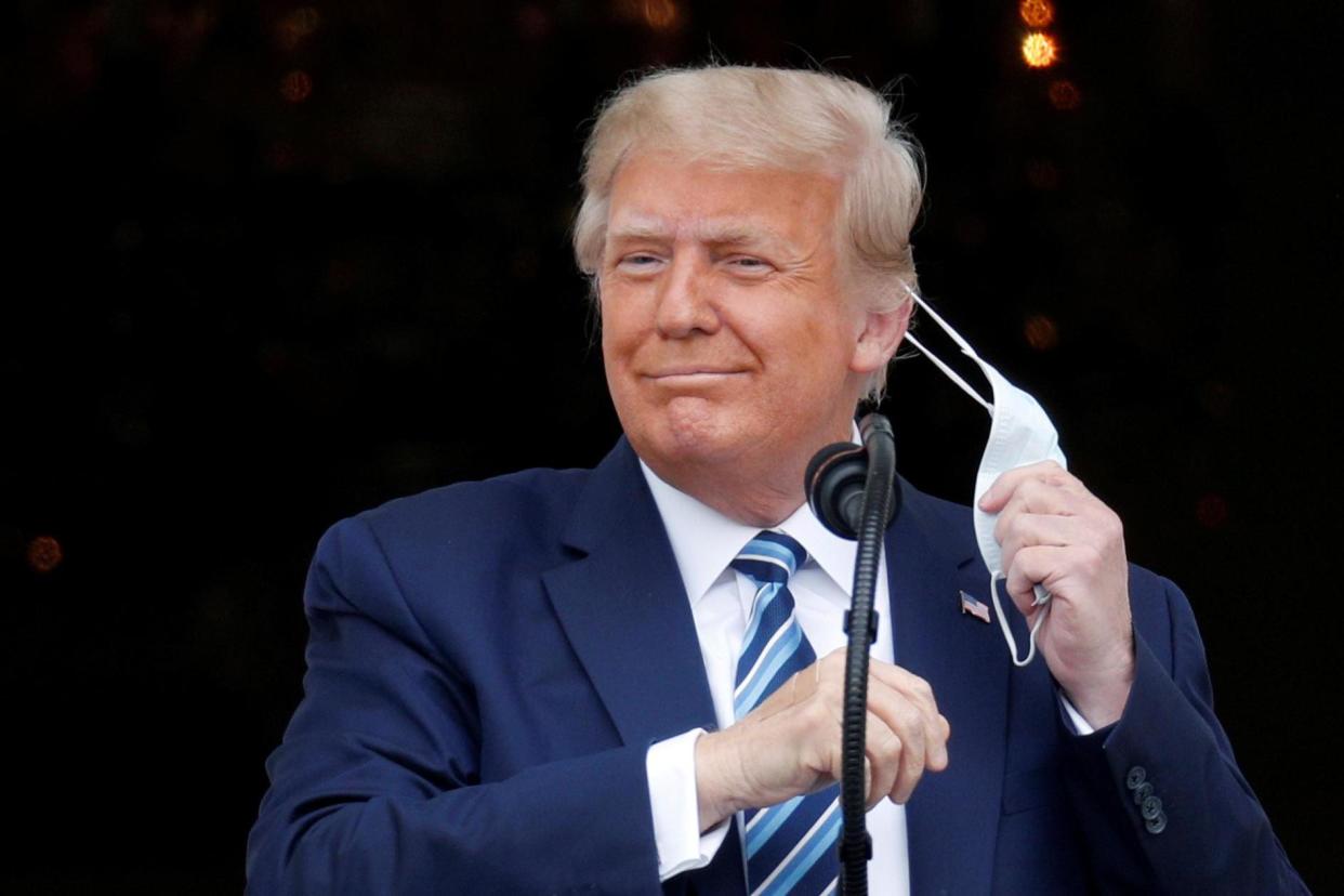 President Donald Trump takes off his face mask as he comes out on a White House balcony to speak to supporters gathered on the South Lawn: REUTERS