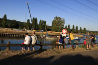 Onlookers wait near the lock of Notre Dame de la Garenne where a Beluga whale is being prepared to be moved, in Saint-Pierre-la-Garenne, west of Paris, France, Tuesday, Aug. 9, 2022. French environmentalists are moving a dangerously think Beluga that had strayed into the Seine River last week to a salt-water river basin to try and save its life. Lamya Essemlali, president of Sea Shepherd France, said the ethereal white mammal measuring 4-meters will be transported to the salty water for "a period of care" by medics who suspect the mammal is sick. (AP Photo/Aurelien Morissard)