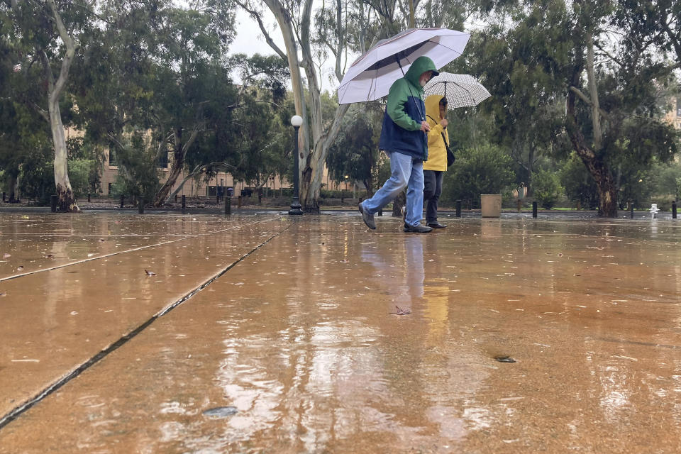 Pedestrians carry umbrellas as they walk in the rain in Stanford, Calif., Saturday, Dec. 31, 2022. A flood watch is in effect across much of Northern California through New Year's Eve. Officials warned that rivers and streams could overflow and urged residents to get sandbags ready. (AP Photo/Jeff Chiu)