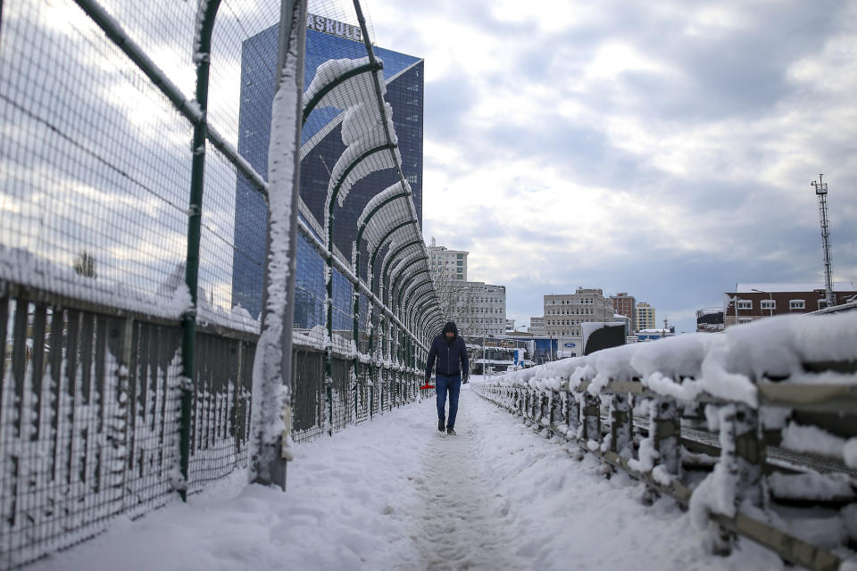 A man walks in a snow-covered street at Istanbul, Tuesday, Jan. 25, 2022. Rescue crews in Istanbul and Athens scrambled on Tuesday to clear throughways that came to a standstill after a massive cold front and snow storms hit much of Turkey and Greece, leaving countless people and vehicles in both cities stranded overnight in freezing conditions.(AP Photo/Emrah Gurel)