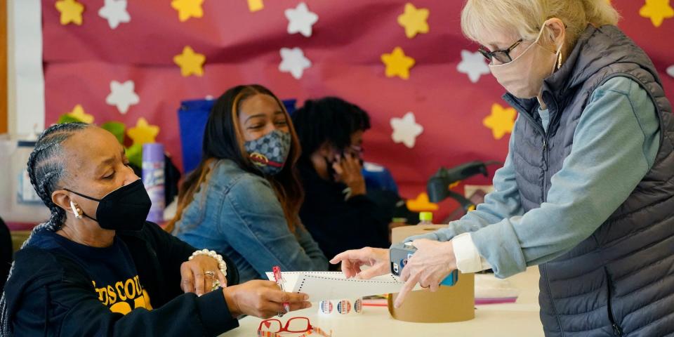 Amy Barnes, left, the Initializing Manager, hands a ballot, an "I Voted in Hinds County" sticker and special pen to a voter in a north Jackson, Miss., precinct, Tuesday, Nov. 2, 2021.