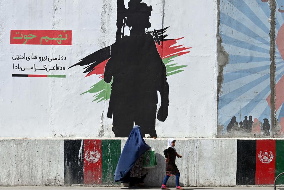 A burqa-clad woman and a girl walk past a mural depicting an Afghan National Army soldier, in Kabul on June 10, 2021.