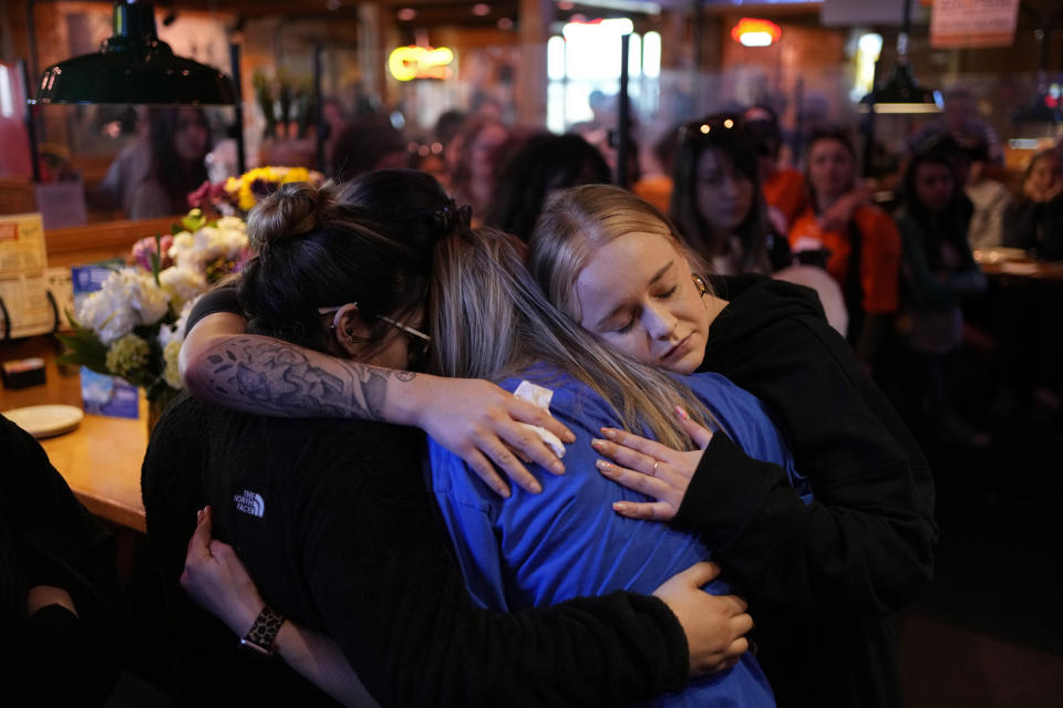 Emily Funderburk, right, embraces friends and coworkers during a memorial for Jackson Zinn at a Texas Roadhouse restaurant, Thursday, March 17, 2022, in Hobbs, New Mexico. Zinn, who worked at the restaurant, was killed with several other student golfers and the coach of University of the Southwest in a crash in Texas. (AP Photo/John Locher)