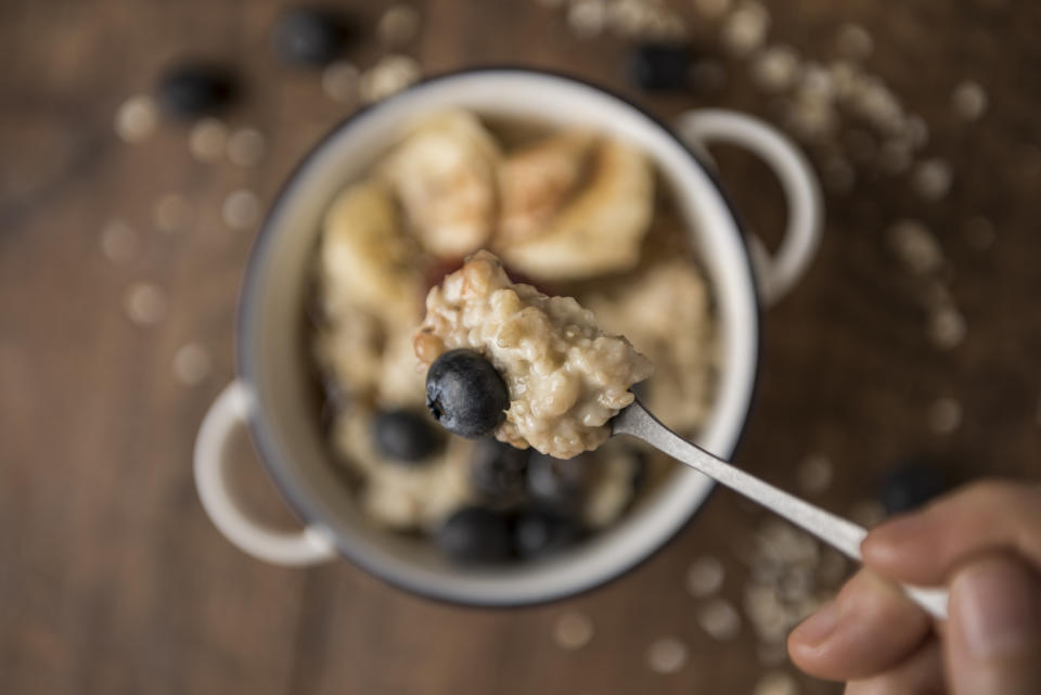 Porridge closeup on a spoon with oat flakes, blueberries and maple syrup. Horizontal. Top view with selective focus.