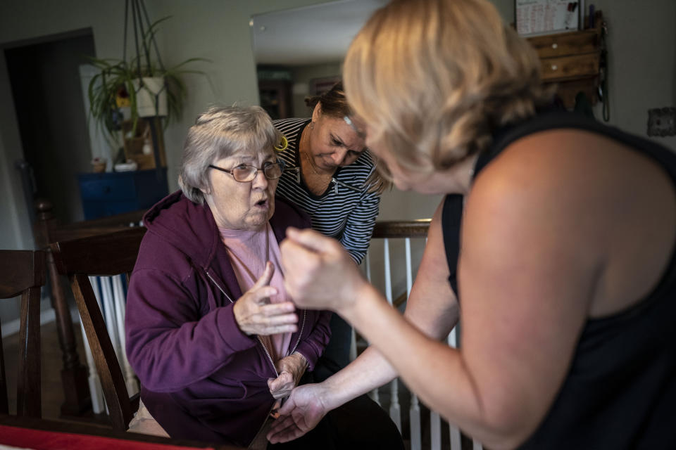 Betty Bednarowski tries to argue with her daughter, Susan Ryder, left, and nursing assistant Arelis Estrella, center, against having her compression stockings put on her legs, Tuesday, Nov. 30, 2021, in Rotterdam Junction, N.Y. (AP Photo/Wong Maye-E)
