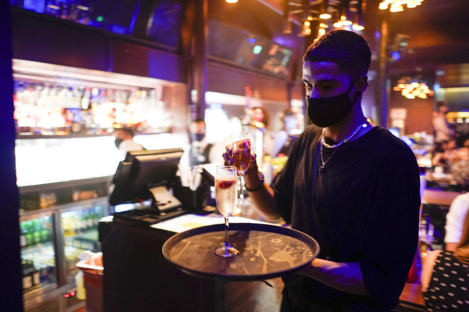 A member of staff wears a face mask as he serves drinks at The Piano Works in Farringdon, in London, on Monday. Photo: AP/Alberto Pezzali