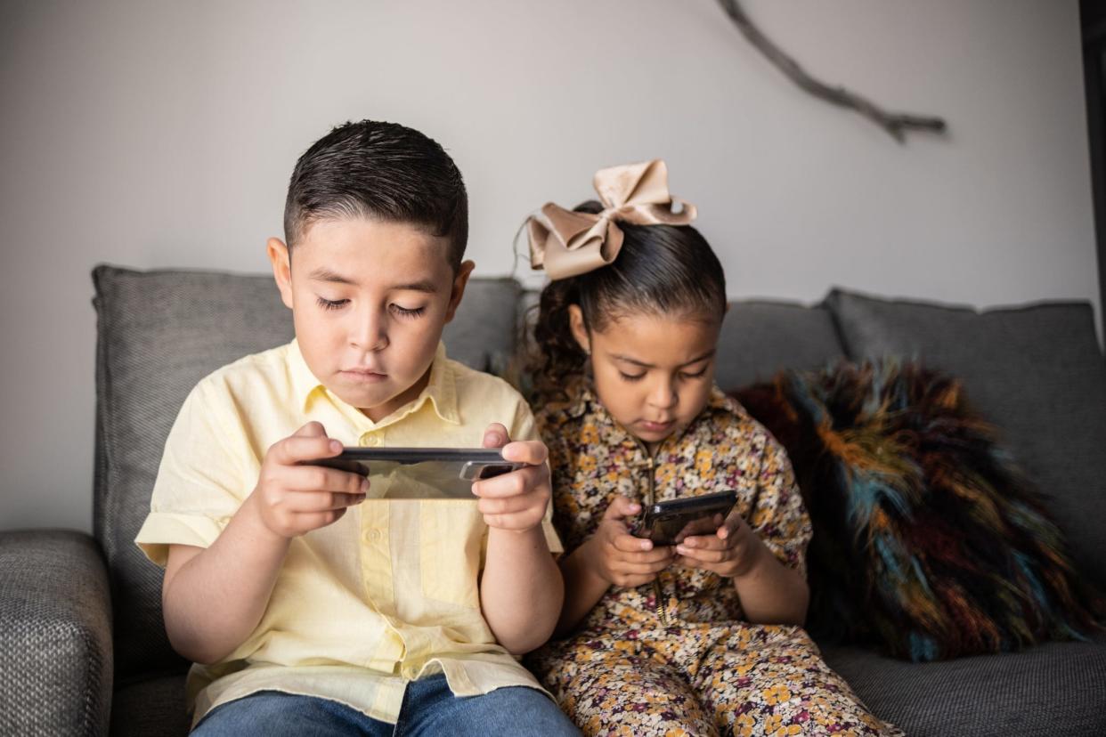 Two siblings look over their mobile devices while sitting on the couch.