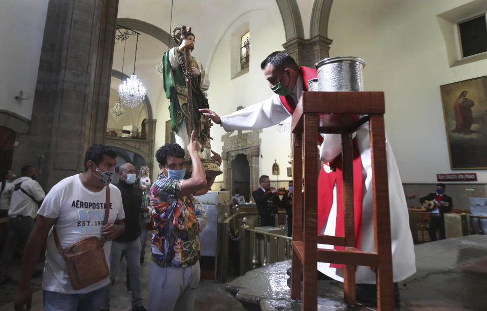 A priest blesses the Saint Jude statue of a devotee at the San Hipolito Catholic church during the annual pilgrimage honoring Jude, the patron saint of lost causes, in Mexico City, Wednesday, Oct. 28, 2020, amid the new coronavirus pandemic. Thousands of Mexicans did not miss this year to mark St. Jude's feast day, but the pandemic caused Masses to be canceled and the rivers of people of other years were replaced by orderly lines of masked worshipers waiting their turn for a blessing. (AP Photo/Marco Ugarte)