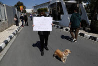 A protestor walks with her dog, holding a banner reading in Greek "The satanist does not represent us" , outside Cyprus' national broadcasting building, during a protest, in capital Nicosia, Cyprus, Saturday, March 6, 2021. The Orthodox Church of Cyprus is calling for the withdrawal of the country’s controversial entry into this year’s Eurovision song context titled “El Diablo”, charging that the song makes an international mockery of country’s moral foundations by advocating “our surrender to the devil and promoting his worship.” (AP Photo/Petros Karadjias)