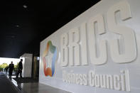 People walk past the BRICS Business Council sign prior the 11th edition of the BRICS Summit, in Brasilia, Brazil, Tuesday, Nov. 12, 2019. The BRICS Summit gathers the group of countries formed by Brazil, Russia, India, China and South Africa, which will take place in the 13th and 14th of this month. (AP Photo/Eraldo Peres)