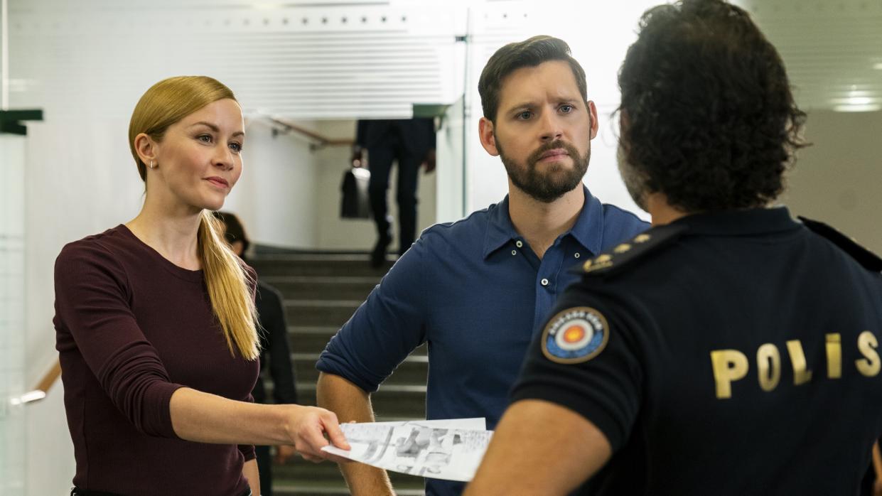 Eva-Jane Willis as Europol Agent Megan “Smitty” Garretson and Luke Kleintank as Special Agent Scott Forrester speaking to a police officer in FBI: International season 2