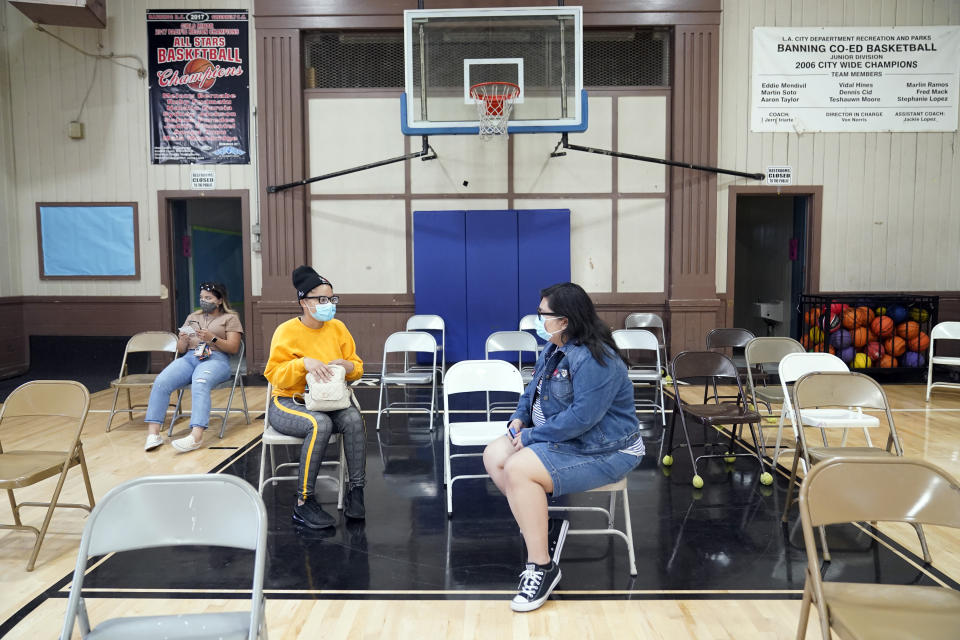 FILE - In this April 13, 2021, file photo, Isis Gardner, center left in yellow, and Esselen Reza, at right, wait in an observation area after receiving a dose of the Pfizer COVID-19 vaccine at the Banning Recreation Center in Wilmington, Calif. With coronavirus shots now in the arms of nearly half of American adults, the parts of the U.S. that are excelling and those that are struggling with vaccinations are starting to look like the nation’s political map: deeply divided between red and blue states. (AP Photo/Marcio Jose Sanchez, File