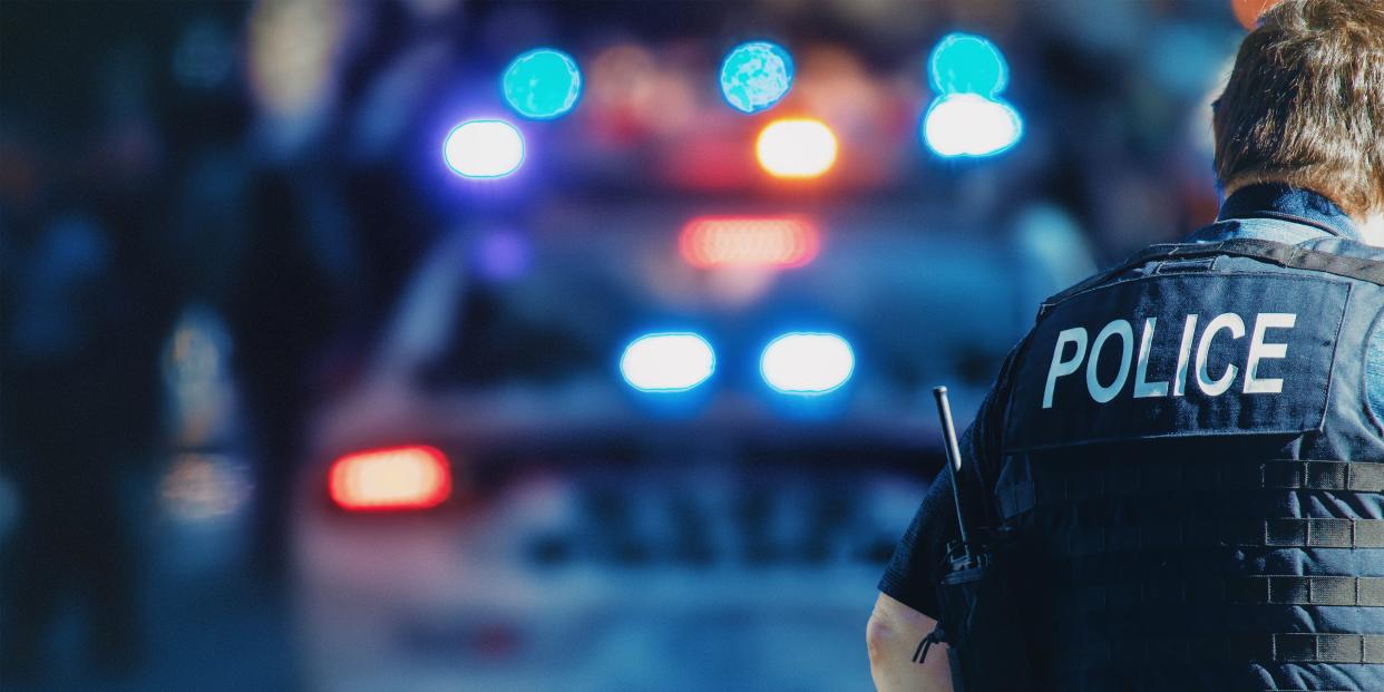 US police officer stands in front of a police car.