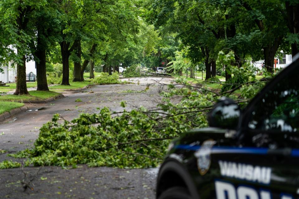 A squad car pulls up next to a street filled with downed tree branches on June 15, 2022 in Wausau, Wis.