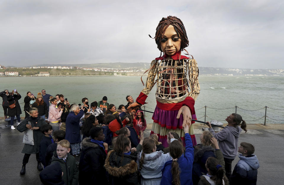 Little Amal, a 3.5-metre-tall puppet of a nine-year-old Syrian girl, is greeted by children from the St. Mary's Primary Academy as she arrives in Folkestone, Kent, as part of the Handspring Puppet Company's 'The Walk'. Picture date: Tuesday October 19, 2021. PA Photo. The puppet started her journey in Turkey on 27 July and has travelled nearly 8,000 km across Greece, Italy, Germany, Switzerland, Belgium and France, symbolising millions of displaced children. (Gareth Fuller/PA via AP)