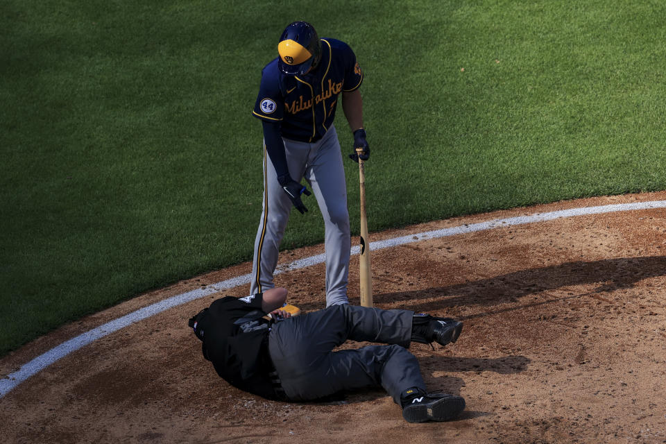 Umpire Ron Kulpa, bottom, lays on the ground after being hit by a pitch as Milwaukee Brewers' Willy Adames (27) checks on him during the sixth inning of a baseball game against the Cincinnati Reds in Cincinnati, Saturday, May 22, 2021. (AP Photo/Aaron Doster)