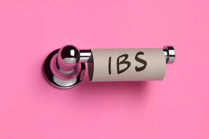 Close up of an empty toilet roll with IBS written on it against pink background