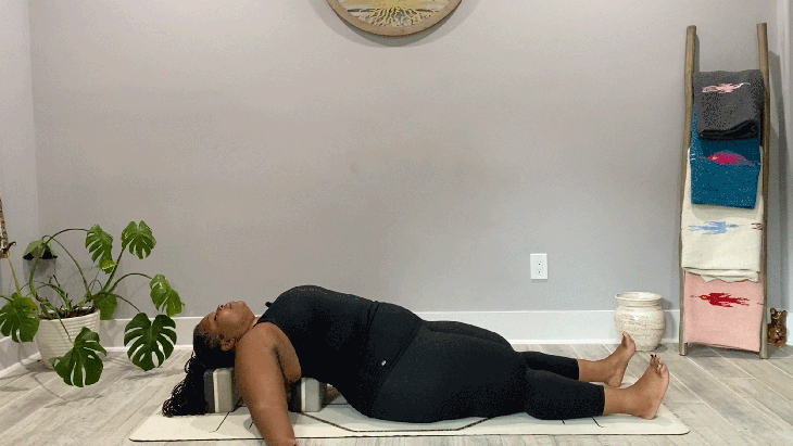 Woman lying on her yoga mat with blocks beneath her upper back in Fish Pose