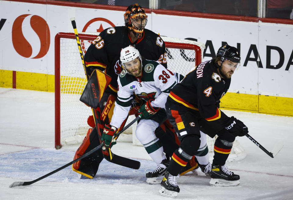 Minnesota Wild forward Ryan Hartman, center, is checked by Calgary Flames defenseman Rasmus Andersson, right, into goalie Jacob Markstrom during the first period of an NHL hockey game Saturday, March 4, 2023, in Calgary, Alberta. (Jeff McIntosh/The Canadian Press via AP)