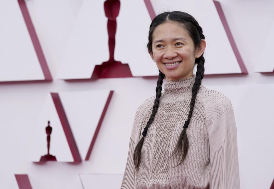 Chloé Zhao in braids wearing a light, high-neck dress.