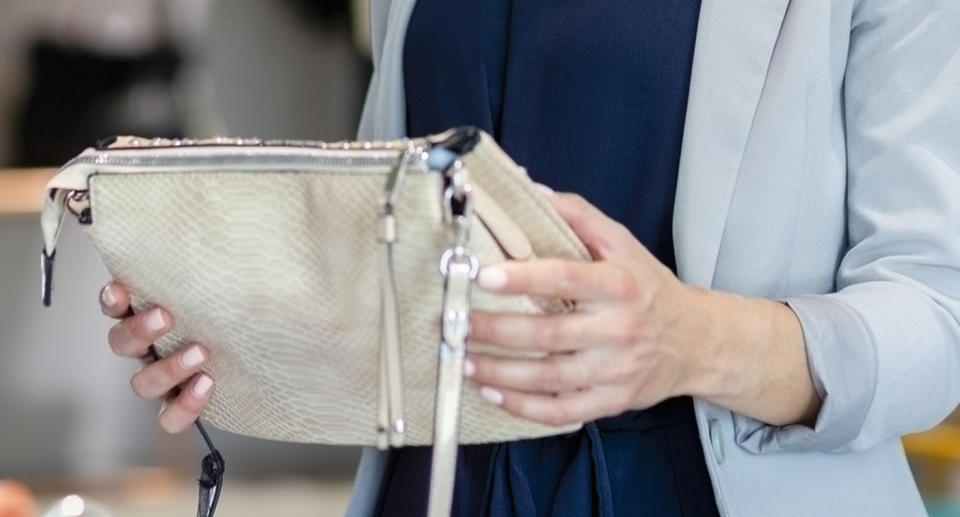 A woman holds a handbag in a store.