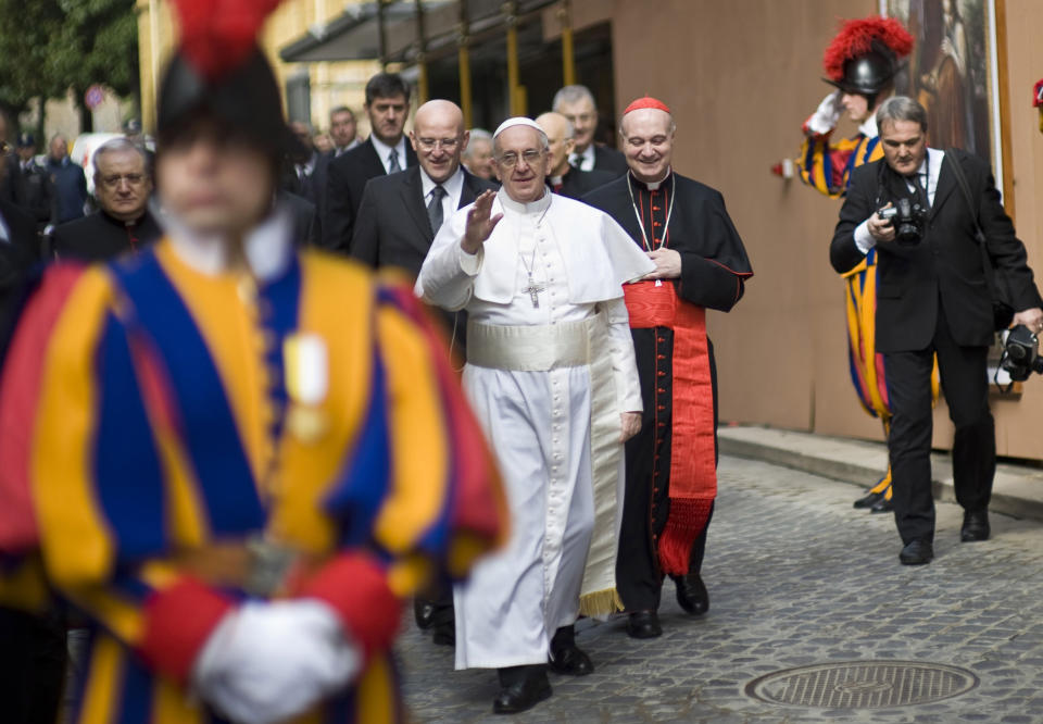 Pope Francis greets faithful at the Vatican, Sunday, March 17, 2013. Pope Francis began his first Sunday as pontiff by making an impromptu appearance to the public from a side gate of the Vatican, startling passersby and prompting cheers, then kept up his simple, spontaneous style by delivering a brief, off-the-cuff homily at the Vatican's tiny parish church. Dressed only in white cassock, Francis waved to the crowd in the street outside St. Anna's Gate and before entering the church, which serves Vatican City State's hundreds of residents, he shook hands of the parishioners and kissed babies. (AP Photo/Antonello Nusca)