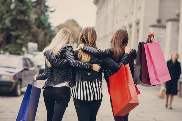 Three women walking down a city street carrying shopping bags.