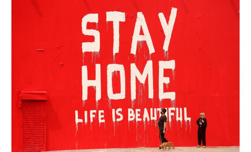 LOS ANGELES, CA - MARCH 31, 2020 - Billy Gross, 35, and girlfriend Kristina Sorensen, 38, right, check out a new mural with a timely suggestion while taking their dog Bear out for a walk along La Brea Avenue in midtown Los Angeles during the coronavirus pandemic on March 31, 2020. Gross, a music manager, and Sorensen, a content development producer, were on their lunch break. (Genaro Molina / Los Angeles Times)